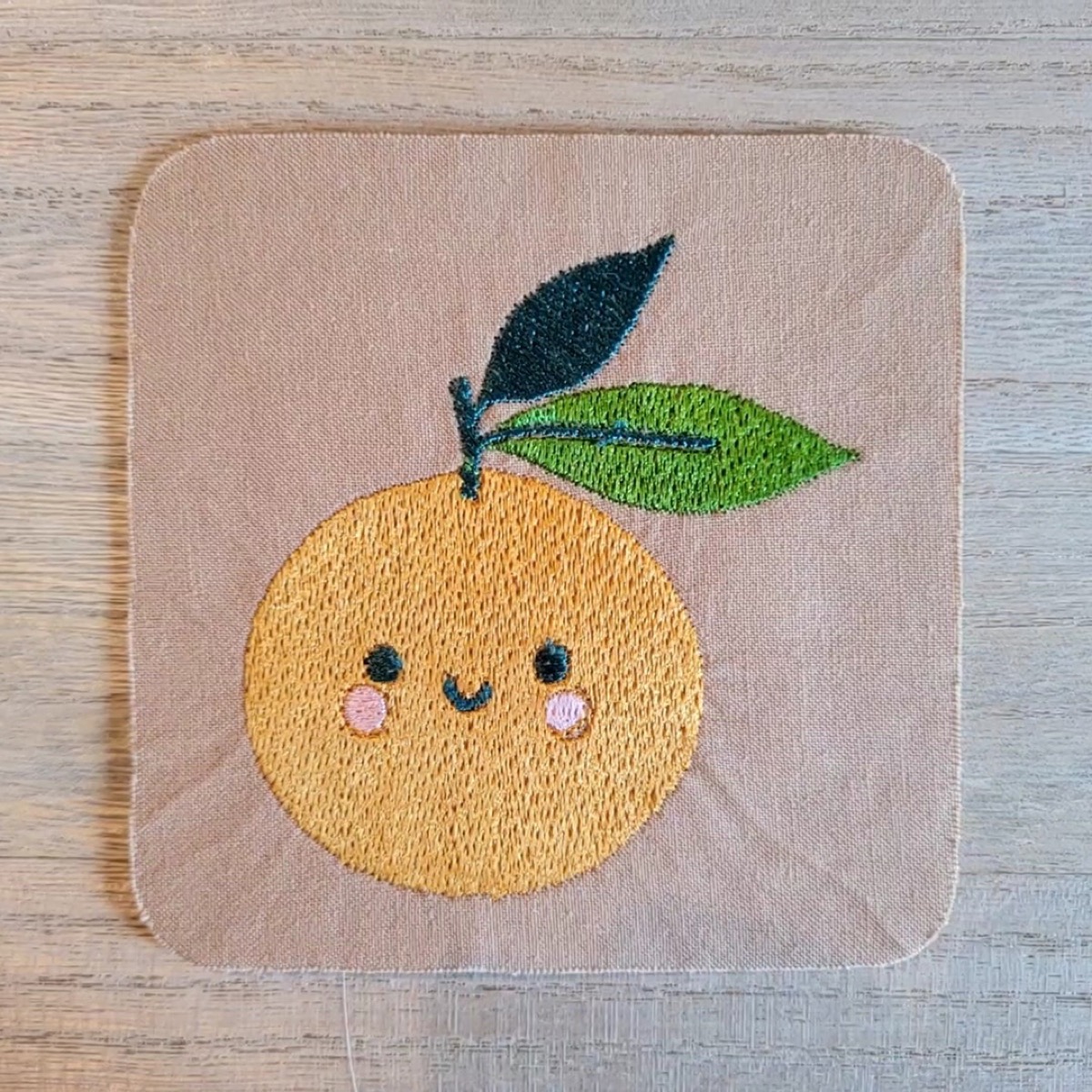 A smiling orange stitched onto pink fabric